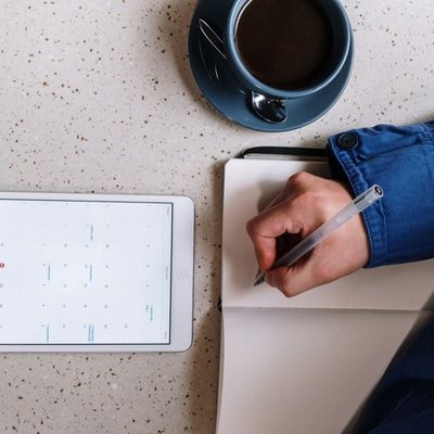 Person checking a calendar on a tablet while taking notes