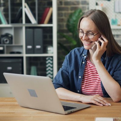 Woman at a desk talking on the phone next to her laptop
