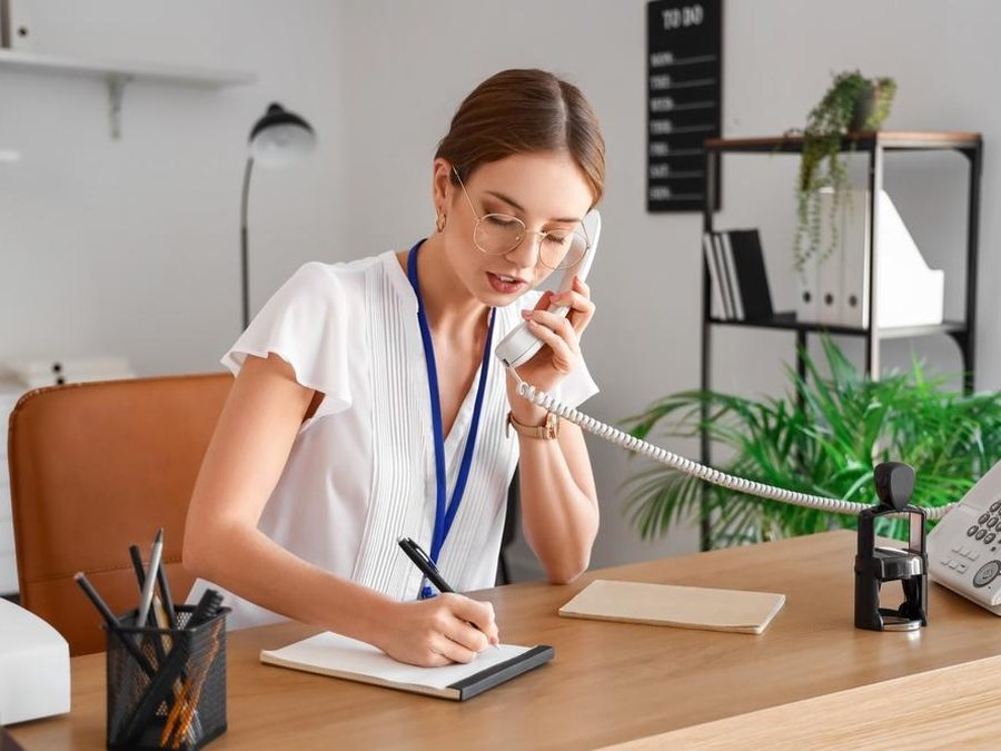 Receptionist on a phone call writing down a message at her desk